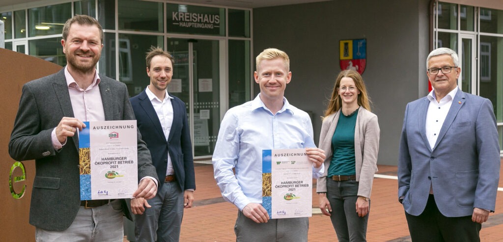 Auf dem Foto sind mehrere Personen zu sehen, die nebeneinander in einer Reihe stehen. Sie halten jeweils Urkunden in den H&auml;nden &ndash; es handelt sich um die Verleihung der &Ouml;koprofit-Zertifikate. Die Gruppe wirkt feierlich und l&auml;chelt in die Kamera. Im Hintergrund ist ein Banner mit dem &Ouml;koprofit-Logo sowie weitere Gestaltungselemente der Veranstaltung zu erkennen. Die Kleidung der Personen ist &uuml;berwiegend gesch&auml;ftlich bzw. festlich, passend zum Anlass.