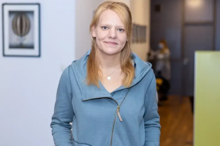 Stephanie Knop. Sie ist Hausmeisterin der Wohnstätte Stade eG. Frau Knoop trägt eine hellblaue Jacke mit Reißverschluss steht in einem Haus und lächelt leicht.