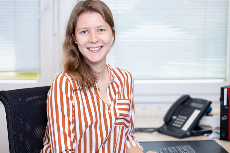 Anneke Moje-Zyber. Sie ist Mitarbeiterin im Bereich Kundenbetreuung der Wohnstätte Stade eG. Frau Moje-Zyber ist früheren Alters, hat schulterlange, braune Haare und trägt eine orange-weiß gestreifte Bluse.