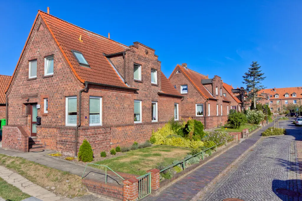 zwei Backstein-Doppelhäusern in der Friedrich-Ebert-Straße Das orangene, spitz zulaufende Ziegeldach wird mit einer Dachgaube verziert. Außerdem sind große, quadratische Fenster zu sehen, welche viel Licht in der Haus lassen. ein Garten grenzt an das Haus. Er wird durch einen flachen Zaun von von der Straße getrennt.