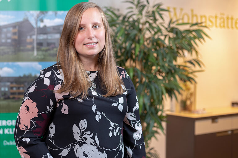 Jandra Lorenzen. Sie ist Mitarbeiterin im Bereich Buchhaltung der Wohnstätte Stade eG. Frau Lorenzen ist früheren Alters, hat Dekoletté-lange, hellbraune Haare und trägt eine Bluse mit Blumen drauf.