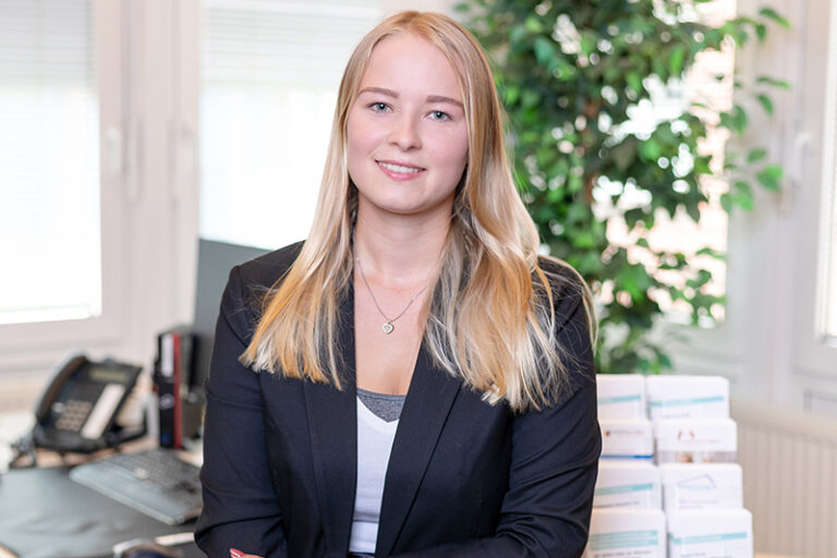 Marie Gamlien. Sie ist Mitarbeiterin in den Bereichen Personal, Digitalisierung und Vermietung der Wohnstätte Stade eG. Frau Gamlien ist früheren Alters, hat blonde brustlange Haare und trägt ein schwarzes Jackett mit einem weißen T-Shirt drunter.