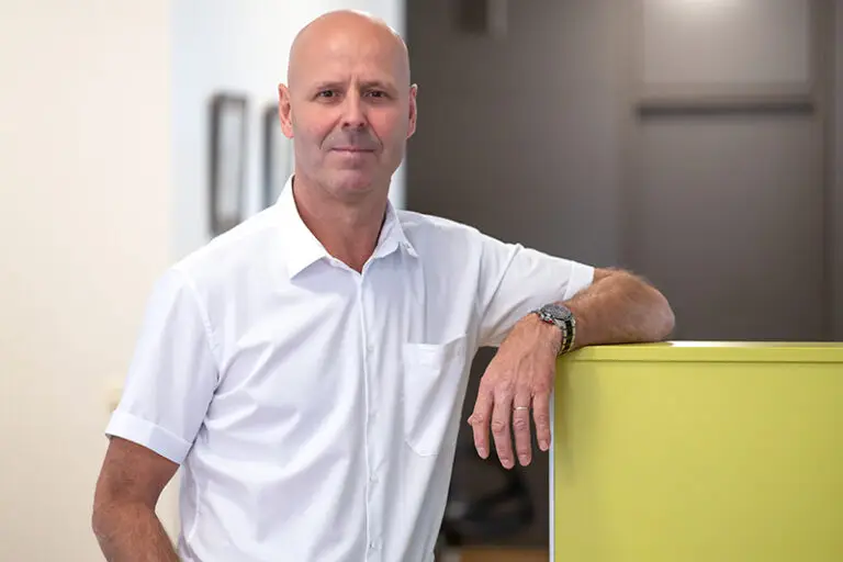 Niels Royke. Er ist Hausmeister der Wohnstätte Stade eG. Herr Royke ist mittleren Alters, hat eine pflegeleichte Frisur und trägt ein weißes kurzärmliges Hemd.