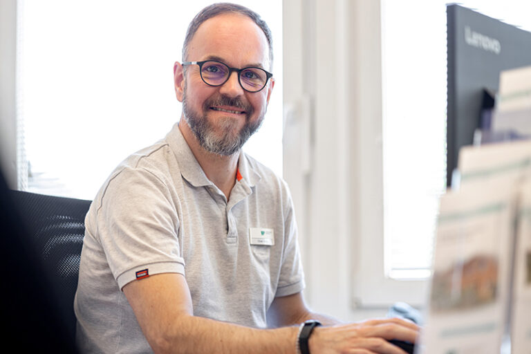 Oliver Helms. Er ist Mitarbeiter im Facility Management der Wohnstätte Stade eG. Herr Helms ist mittleren Alters, hat einen Kurzhaarschnitt und trägt eine Brille, sowie ein kurzärmliges weißes Polo-T-Shirt.
