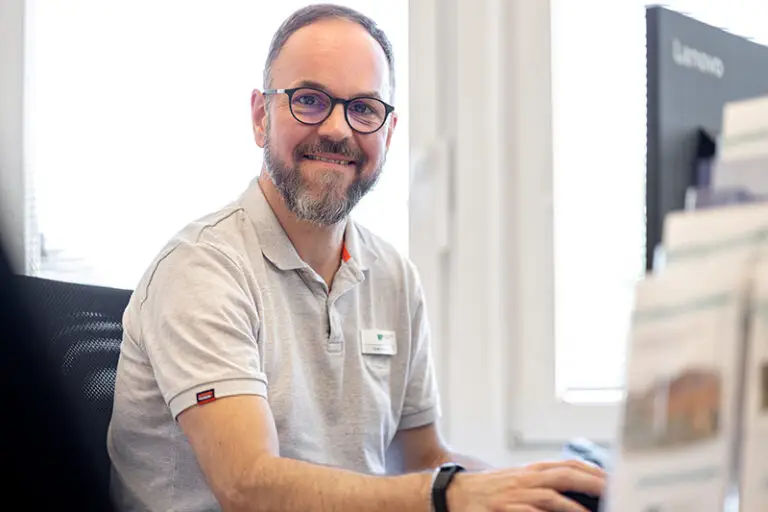 Oliver Helms. Er ist Mitarbeiter im Facility Management der Wohnstätte Stade eG. Herr Helms ist mittleren Alters, hat einen Kurzhaarschnitt und trägt eine Brille, sowie ein kurzärmliges weißes Polo-T-Shirt.