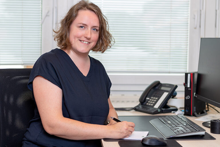 Sarah Feuersänger. Sie ist Mitarbeiterin im Bereich Buchhaltung der Wohnstätte Stade eG. Frau Feuersänger ist mittleren Alters, hat schulterlange, gewellte Haare und trägt eine dunkelblaue, kurzärmelige Bluse.