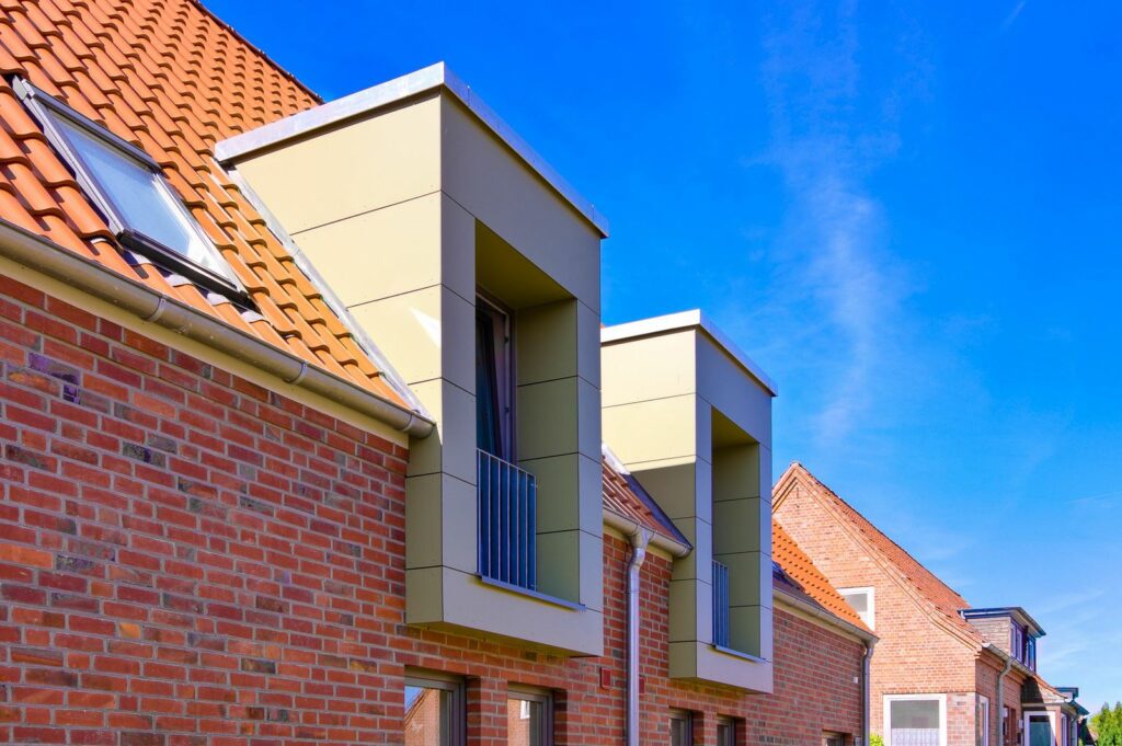 Moderne Backsteinh&auml;user mit roten Ziegeld&auml;chern und rechteckigen Dachgauben unter einem strahlend blauen Himmel, die zeitgen&ouml;ssische architektonische Gestaltungselemente zeigen.