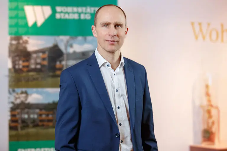 Dr. Christian Pape. Er ist Vorstand der Wohnstätte Stade eG. Herr Pape ist mittleren Alters, hat einen Kurzhaarschnitt und trägt einen blauen Anzug, darunter ein helles Hemd.