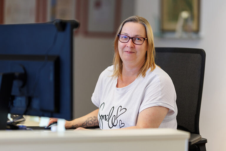 Susann Pehmöller. Sie ist Mitarbeiterin in den Bereichen Mitgliederverwaltung, Empfang und Buchhaltung der Wohnstätte Stade eG. Frau Pehmöller ist mittleren Alters, hat schulterlange blonde Haare und trägt eine Brille, sowie ein weißes T-Shirt.