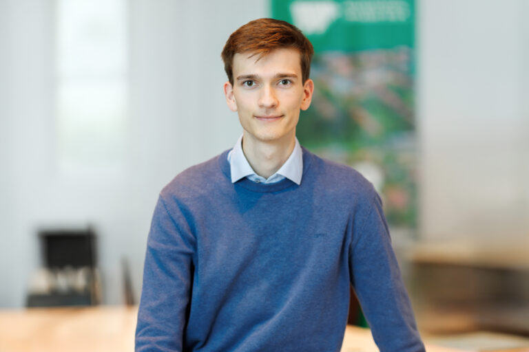 Finn Dittmer. Er ist Mitarbeiter im Bereich Kundenbetreuung der Wohnstätte Stade eG. Herr Dittmer ist früheren Alters, hat einen braunen Kurzhaarschnitt und trägt einen blauen Pullover, worunter der Kragen eines hellblauen Hemdes hervorschaut.