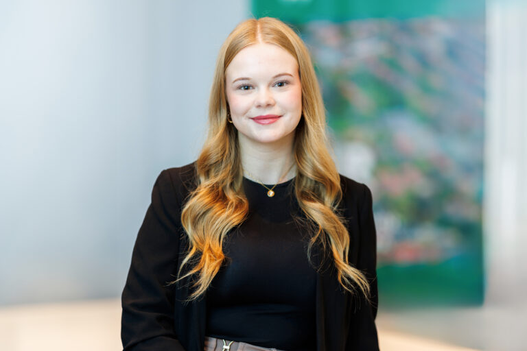 Lara Saathoff. Sie ist Auszubildende der Wohnstätte Stade eG. Frau Saathoff ist früheren Alters, hat hüftlange blonde Haare und trägt ein schwarzes Jackett mit einem schwarzen Shirt darunter.