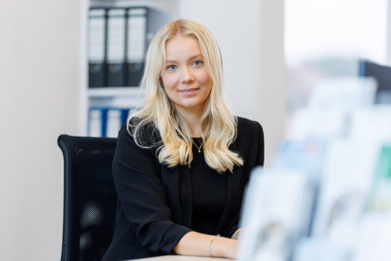 Carolin Meiling. Sie ist eine Mitarbeiterin im Bereich Vermietung der Wohnstätte Stade eG. Frau Meiling ist früheren Alters, hat Dekolleté-langes, blondes Haar und trägt eine schwarze Bluse mit Dreiviertelarmen.