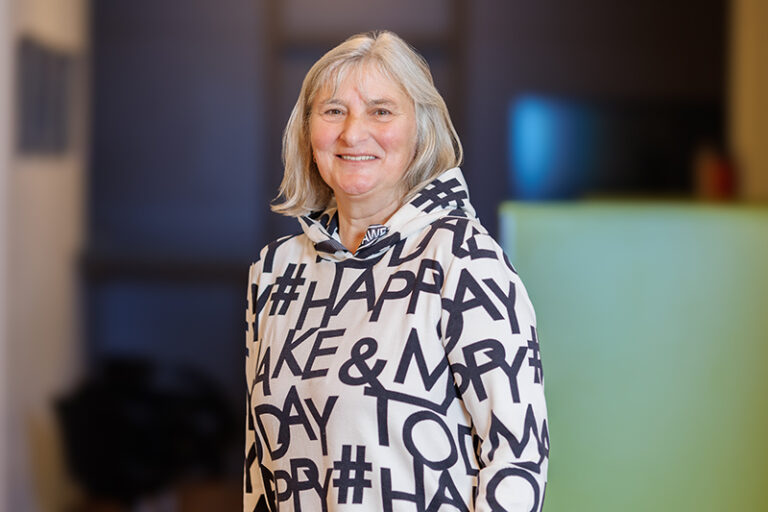 Ute Birkl. Sie ist Mitarbeiterin im Bereich Seniorenbetreuung in dem Lerchenweg 75 der Wohnstätte Stade eG. Frau Birkl ist mittleren Alters, hat schulterlange blonde Haare und trägt einen weißen Pullover mit Aufdruck.