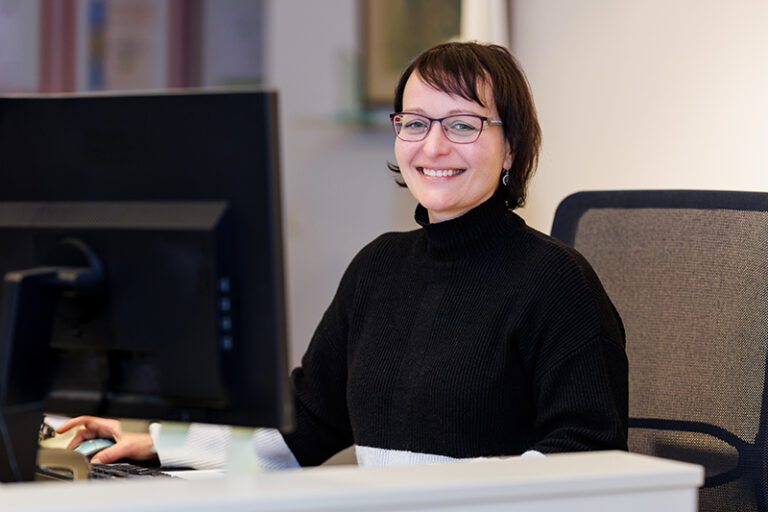 Silvana Weber. Sie ist Mitarbeiterin in den Bereichen Mitgliederverwaltung und Empfang der Wohnstätte Stade eG. Frau Weber ist mittleren Alters, hat einen dunkelbraunen Bob und trägt eine Brille, sowie einen schwarzen Rollkragenpullover.